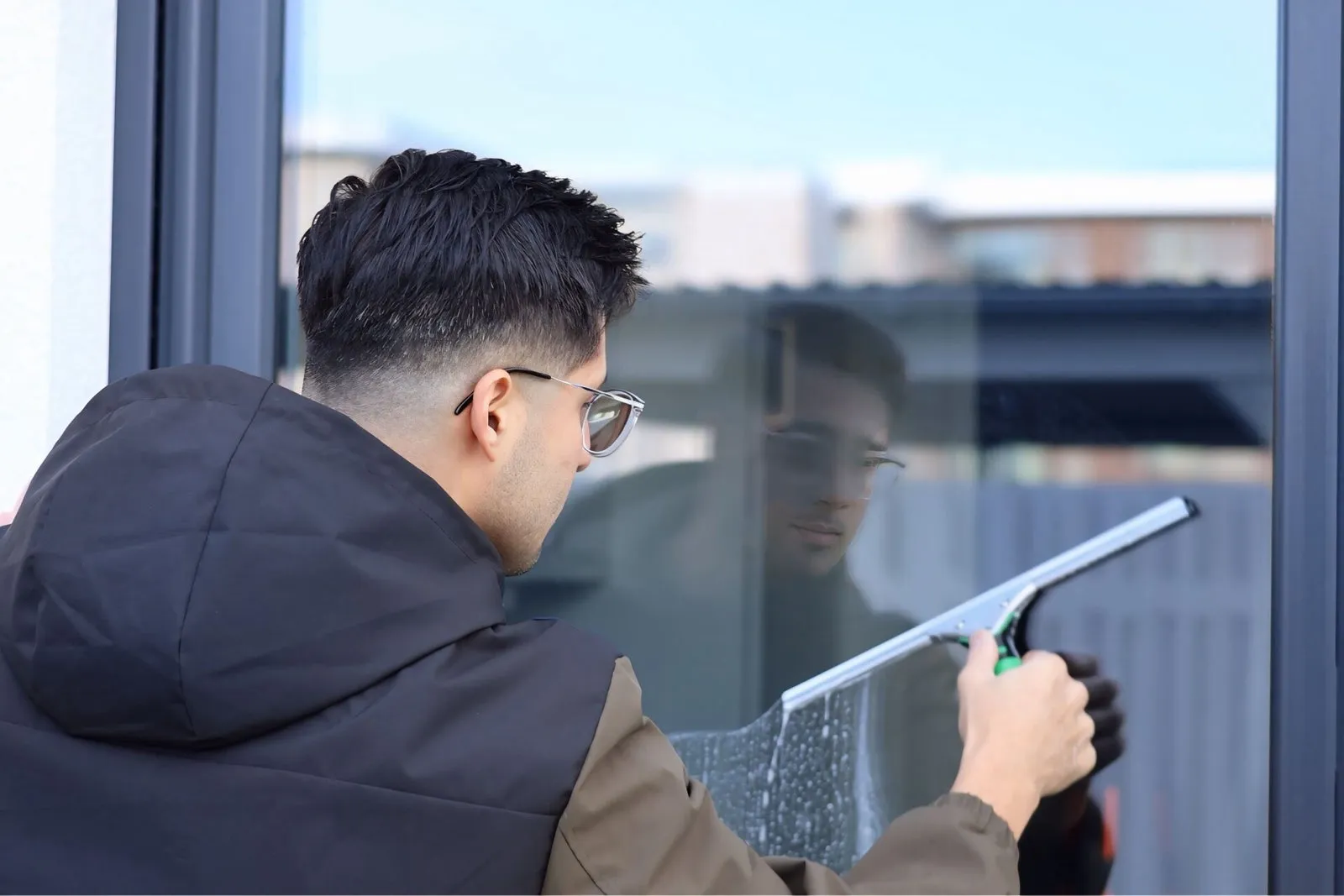 Ahmad Atayi zieht eine Glasfläche mit dem Fensterwischer streifenfrei ab